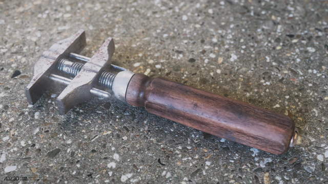 An old sturdy french wrench with a wooden handle lying on a concrete floor.
