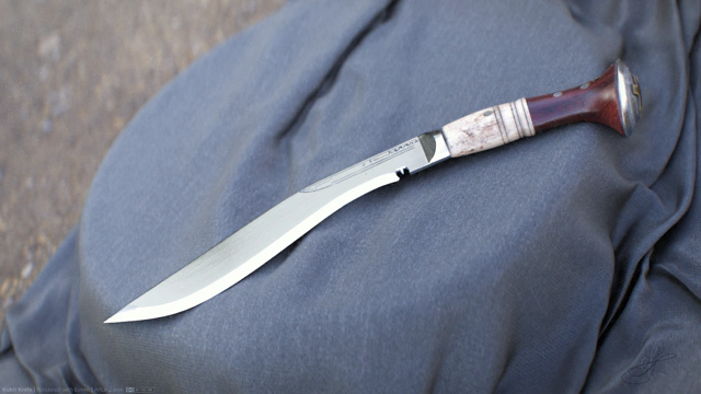 Kukri knife lying on a tree stump. The stump is draped with a bluish cloth. There's an unfocused forest ground visible in the background.